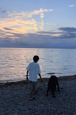 夕暮れの浜辺を並んで歩く子どもと犬
