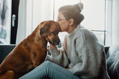 落ち込んだ犬と向かい合ってキスする女性