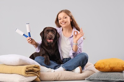粘着ローラーを持ちながらベッドに座る犬と女の子