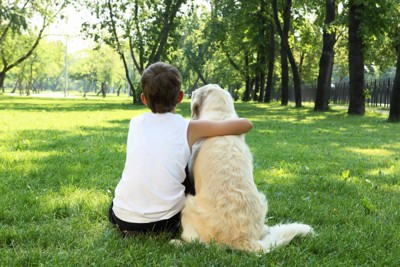 犬と肩を組んで座っている男の子の後ろ姿