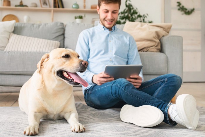 タブレット視聴中の男性のとなりに座る大型犬