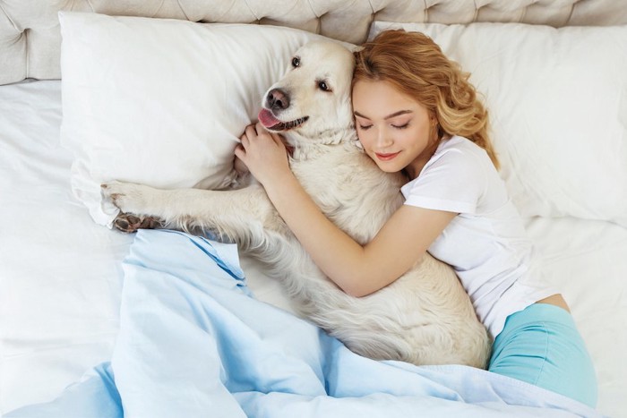 ベッドで愛犬と一緒に寝る女性