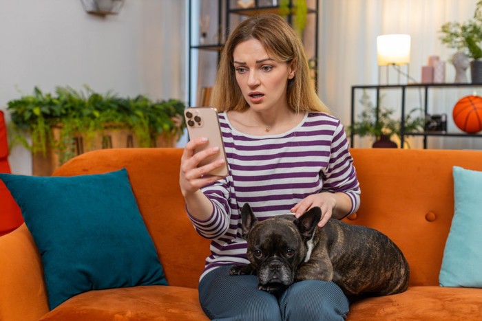 犬とスマホを見て驚く女性