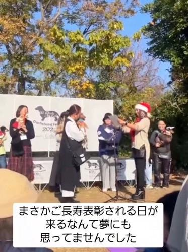 賞状を読み上げる女性の前に立つ飼い主と犬