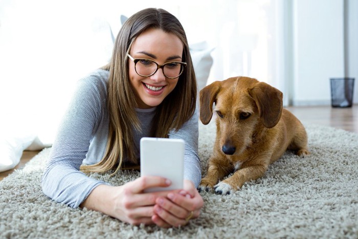 女性とスマホを見る犬