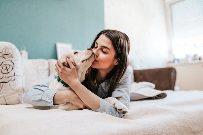 ベッドの上で犬にキスをする女性