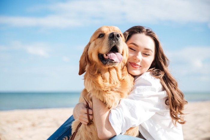 海を背景に砂浜で犬を抱きしめる女性