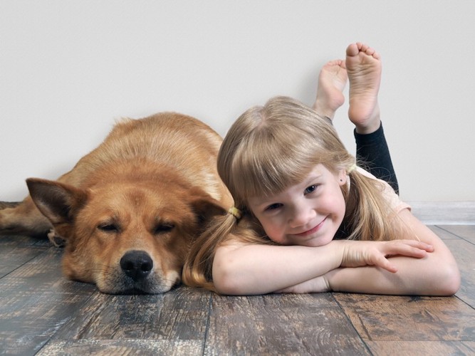 床に寝そべる犬と一緒に寝そべる笑顔の子供