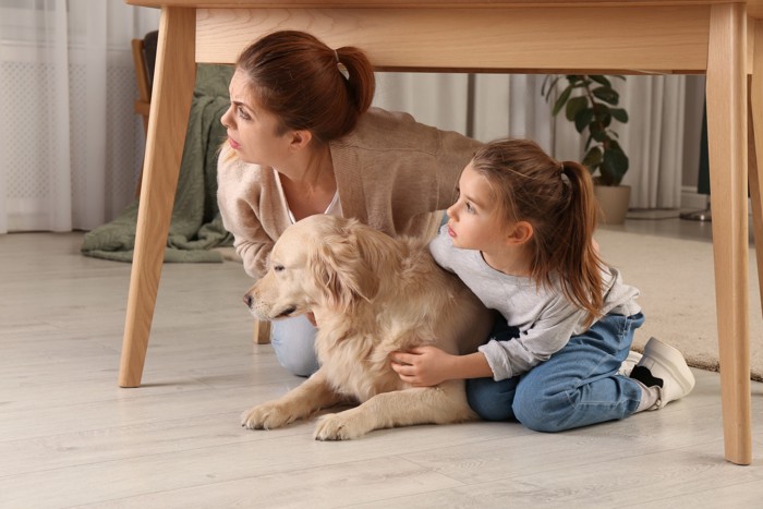 地震から身を守るためにテーブルの下に隠れる親子と犬