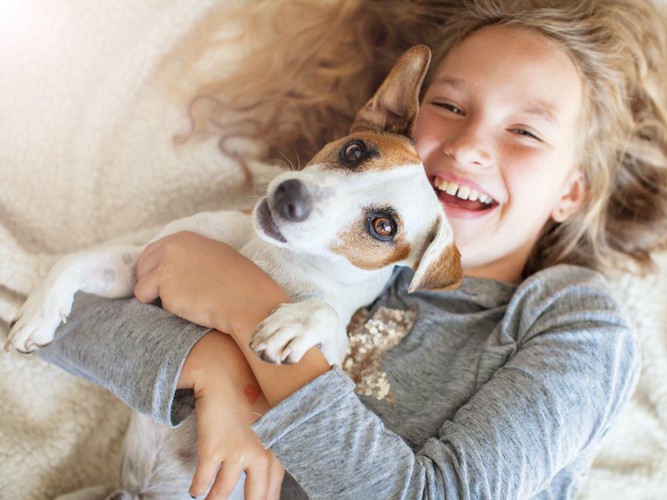 犬を抱きしめて寝転がる笑顔の少女