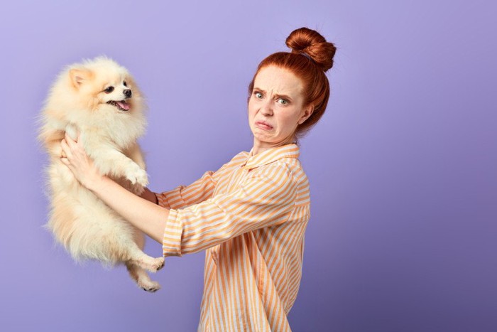 しかめっ面の女性と抱っこされる犬