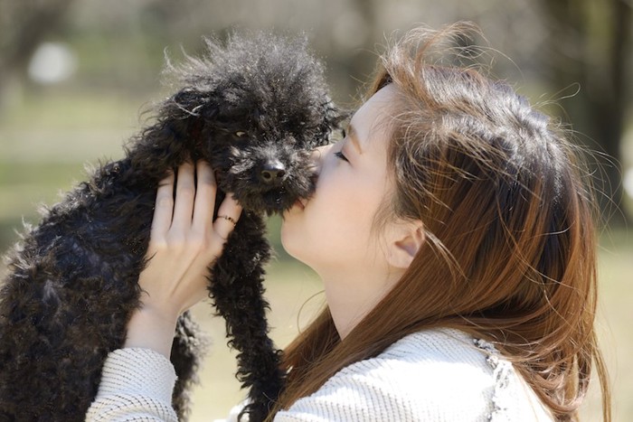 黒いトイプードルを抱き上げてキスする女性