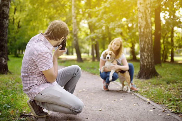 犬を抱えた女性を撮影する男性