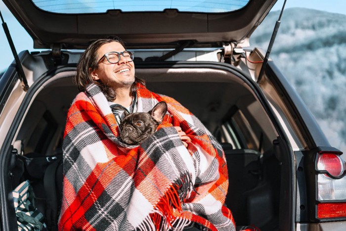 車のトランクで飼い主さんに抱っこされる犬