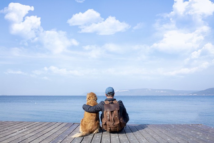 並んで座って海を見つめる男性と犬の後ろ姿