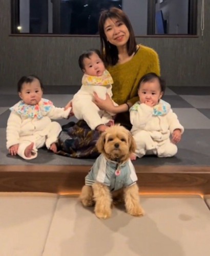 3人の赤ちゃんと女性の前に座ってカメラを見つめる犬