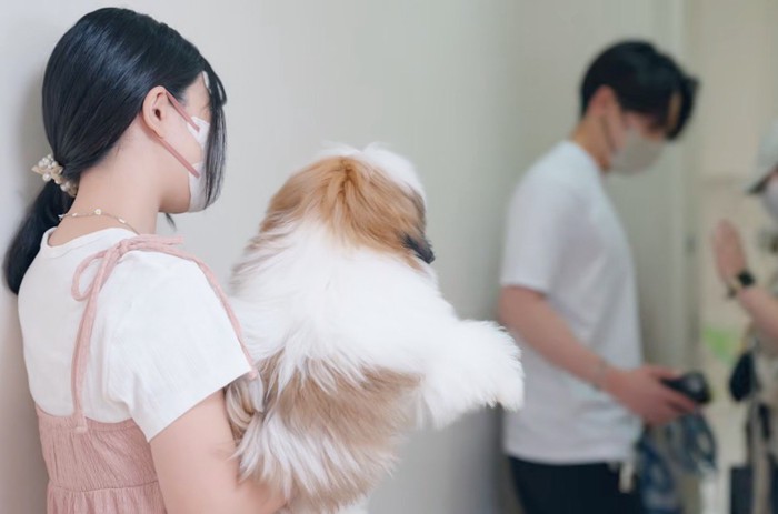 店を出る飼い主を、トリマーに抱っこされて見送る子犬