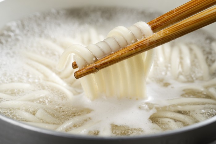 鍋で茹でているうどんを箸で持ち上げている様子