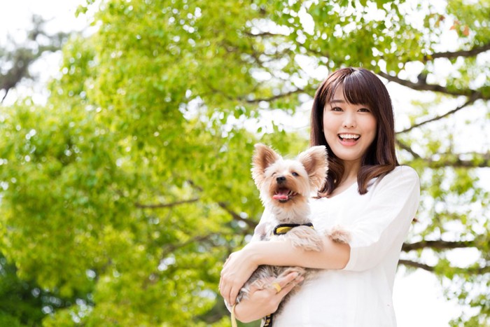 緑を背景に抱っこされる犬と女性