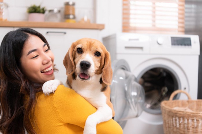 洗濯機のそばで飼い主さんい抱っこされる犬