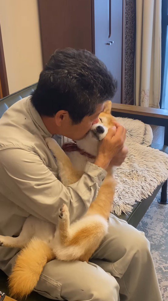 男性に顔を寄せられて目を細める犬