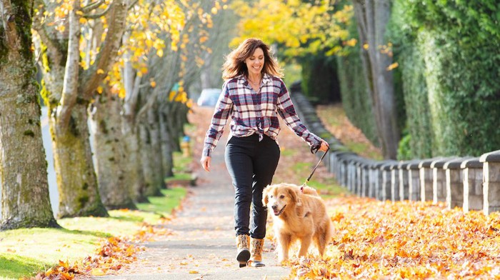 落ち葉の中を楽しそうに散歩する女性と犬