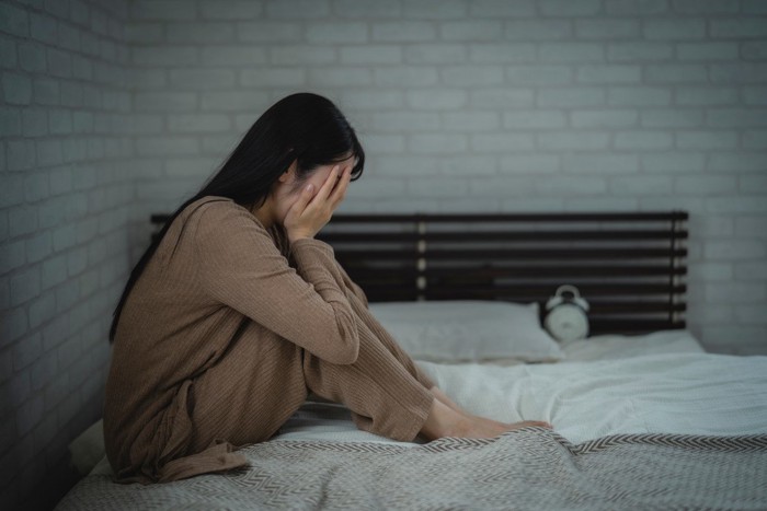ベッドの上で顔を覆う女性