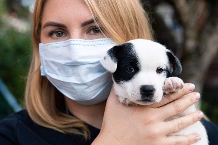 子犬を抱くマスク姿の女性