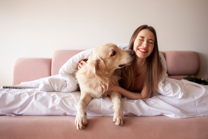 ベッドで女性に顔を近づける犬