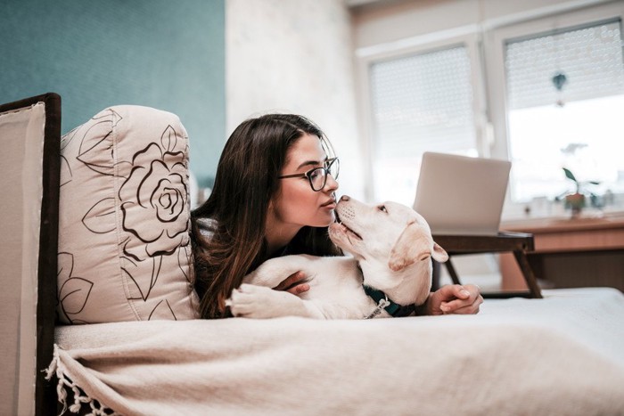 寝転がる女性の顔を舐めようとする犬