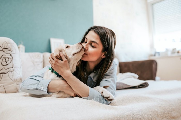 ベッドで犬にキスをする女性