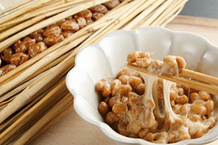 藁に入った納豆と小皿から箸で納豆を持ち上げている様子