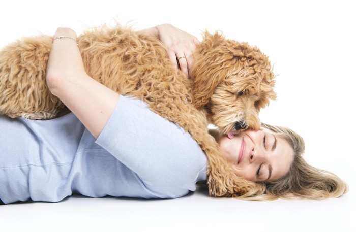 横になった女性の上に乗っかってキスする犬