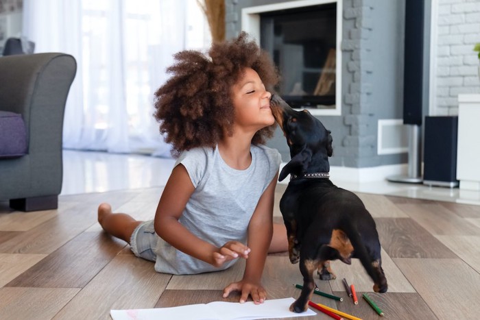 お絵かきをしている子どもの口元を舐める犬