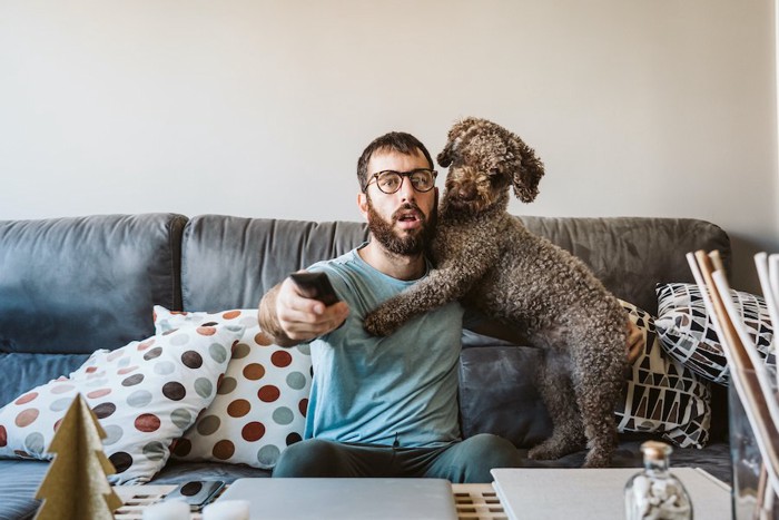 テレビを見ようとしている男性に抱きついて甘える犬