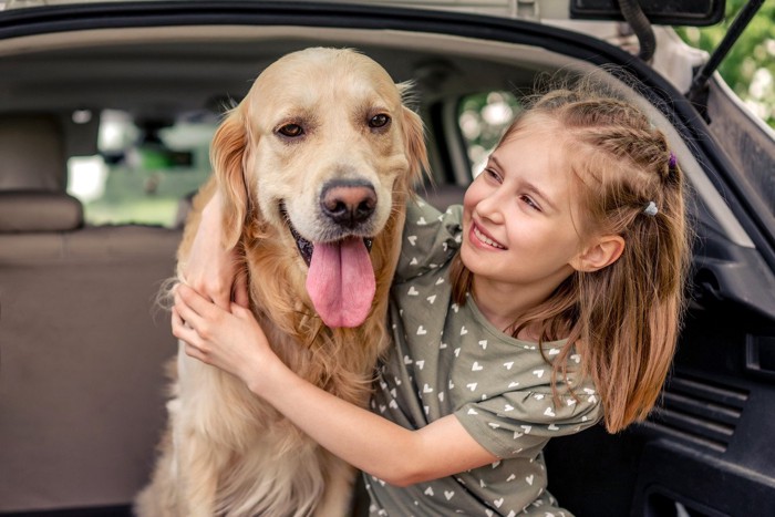 車のトランクに座って微笑む少女と犬