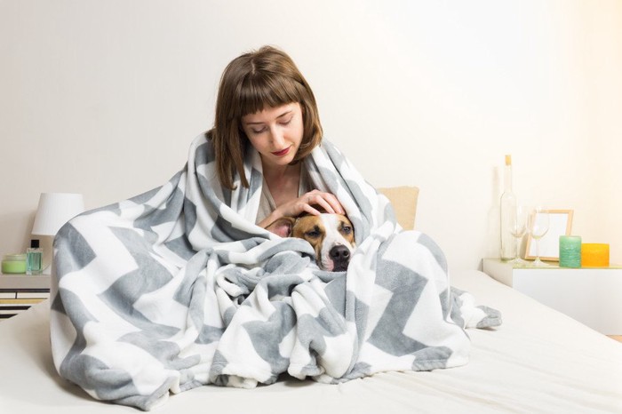 布団にくるまる女性と犬