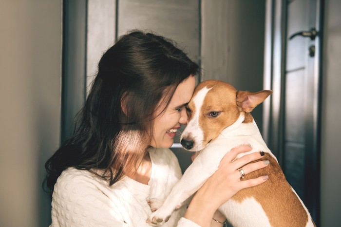 白茶の犬と頭を合わせて抱っこする女性