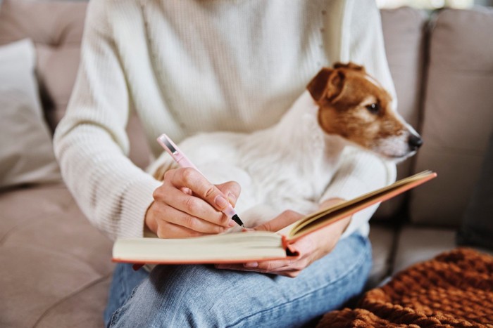 犬を膝の上に抱っこしながら何かを書く女性