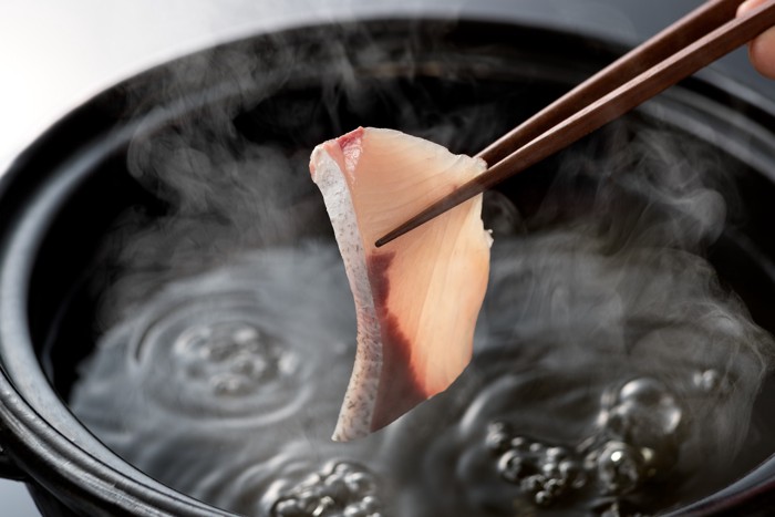 箸でつかんだブリの切り身を鍋で茹でるところ