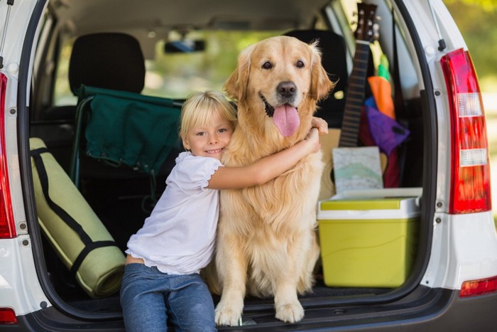 旅先の車のトランクで笑顔の少女と犬