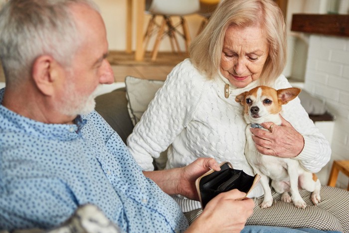 空っぽの財布を見てがっかりする老夫婦に抱かれる犬