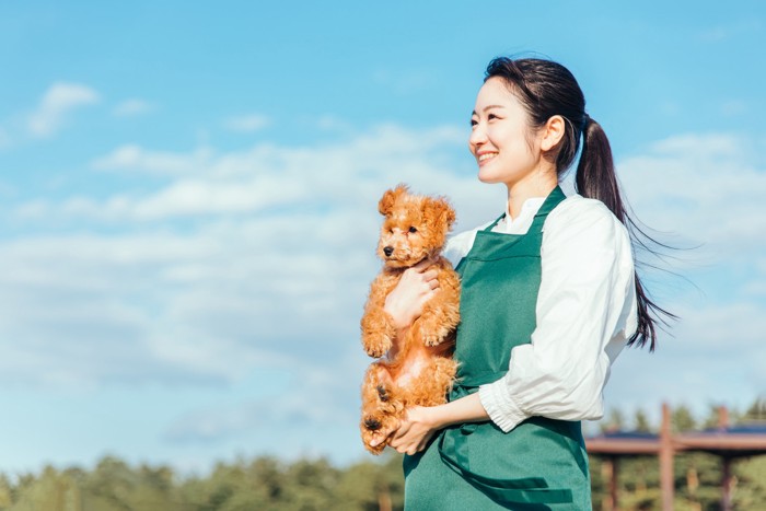 犬を抱きかかえながら遠くを見つめるトリマー