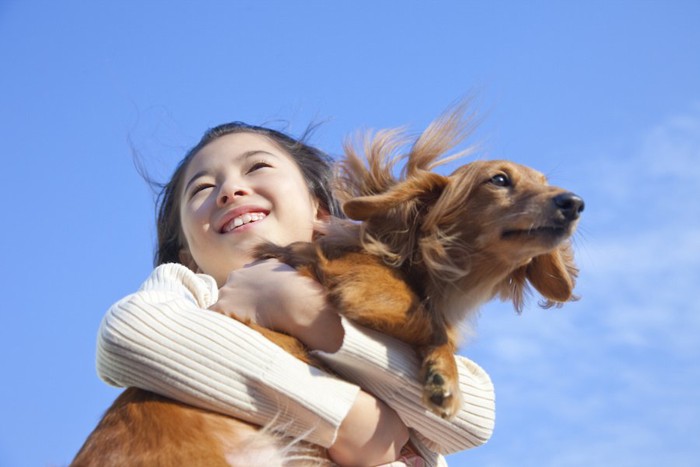 青空のもとで犬を抱きしめている女の子