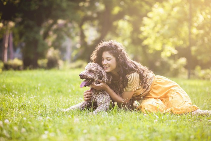 芝生の上に伏せる犬を撫でる女性