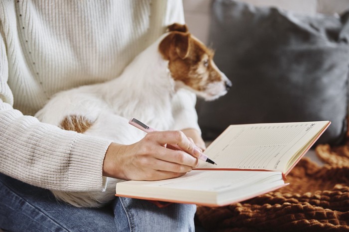 犬を抱っこして書き物をする